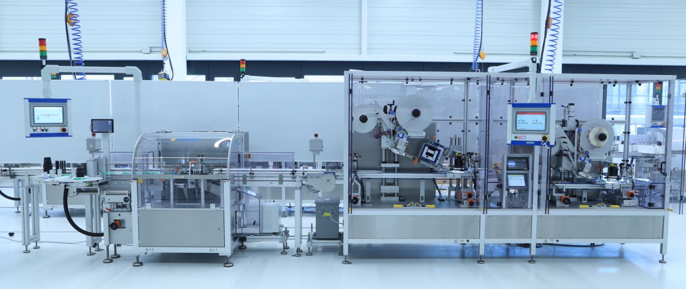 Automatisierte Produktionslinie mit mehreren Maschinen, Bildschirmen und Sicherheitsvorrichtungen in einer modernen Fabrikumgebung.