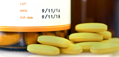 Gelbe Tabletten liegen neben einem Fläschchen mit einem Etikett, das das Herstellungsdatum und das Ablaufdatum zeigt.