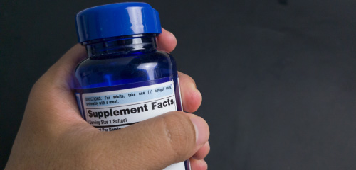Eine Hand hält eine blaue Flasche mit Nahrungsergänzungsmitteln, auf dem Etikett sind die Supplement-Fakten zu sehen.