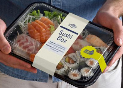 Eine Person hält eine Sushi-Box mit verschiedenen Sushi-Sorten, darunter Lachs, Thunfisch und Gemüse, verpackt in einer transparenten Schale.