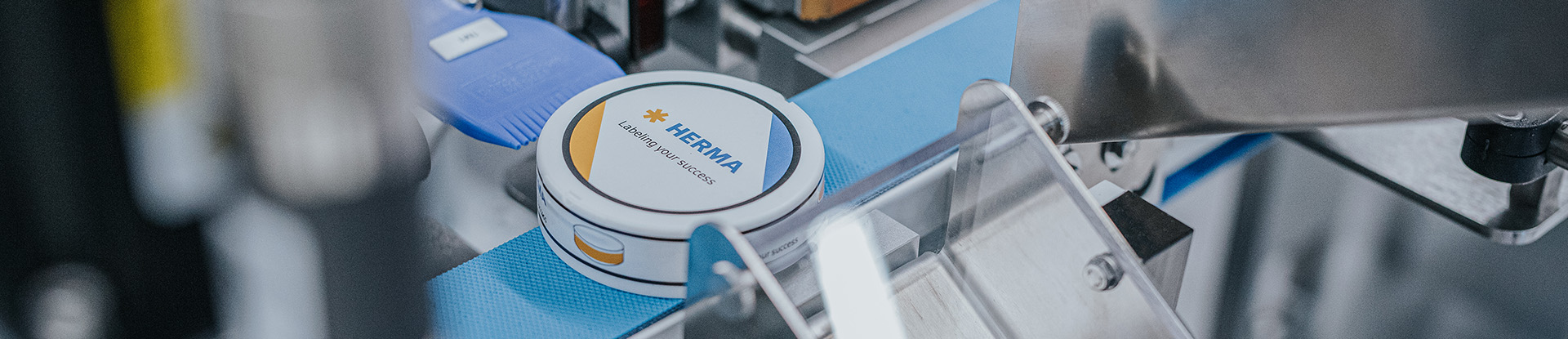 Eine Dose mit dem Logo von "HERMIA" auf einem Förderband in einer Produktionsumgebung.