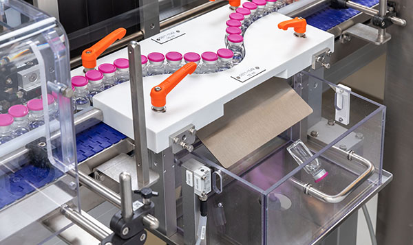 Automatisierte Verpackungsmaschine mit Fläschchen auf einem Förderband und einem Karton, der zur Verpackung bereitsteht.