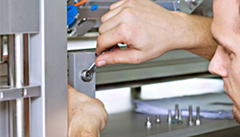 Ein Techniker zieht eine Schraube an einer Metallkonstruktion mit einem Schraubenschlüssel an. Werkzeuge und Teile sind im Hintergrund sichtbar.