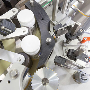 Maschine zur Etikettierung von Flaschen, mit verschiedenen mechanischen Komponenten und Sensoren zur präzisen Handhabung.