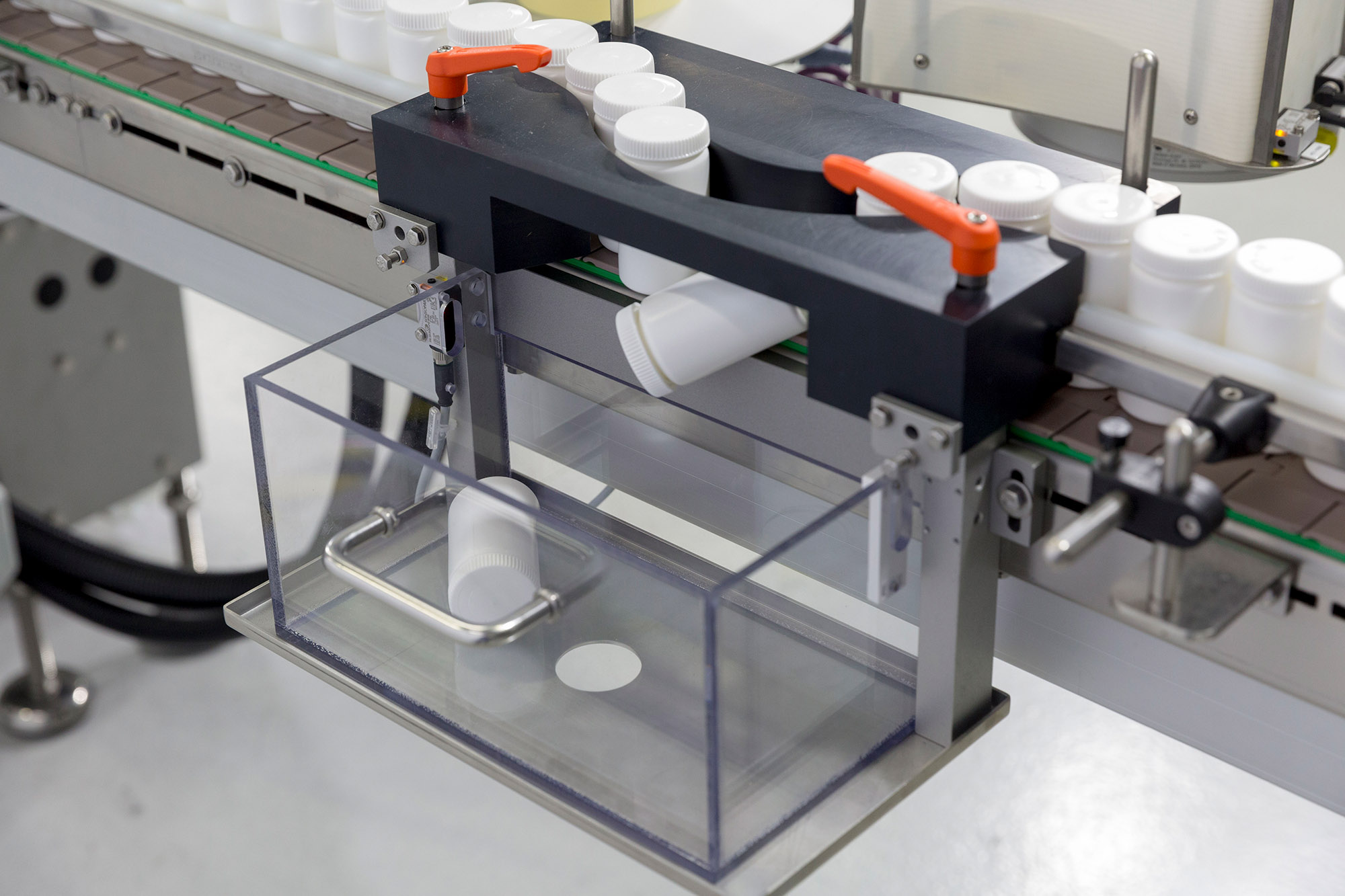 Automatisierte Verpackungsmaschine mit einem transparenten Behälter, der Behälter von einem Förderband aufnimmt.