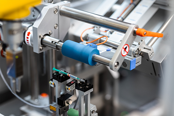 Automatisierte Maschinenkomponenten mit einem blauen Zylinder und verschiedenen Greifern zur Handhabung von Objekten in einer industriellen Umgebung.