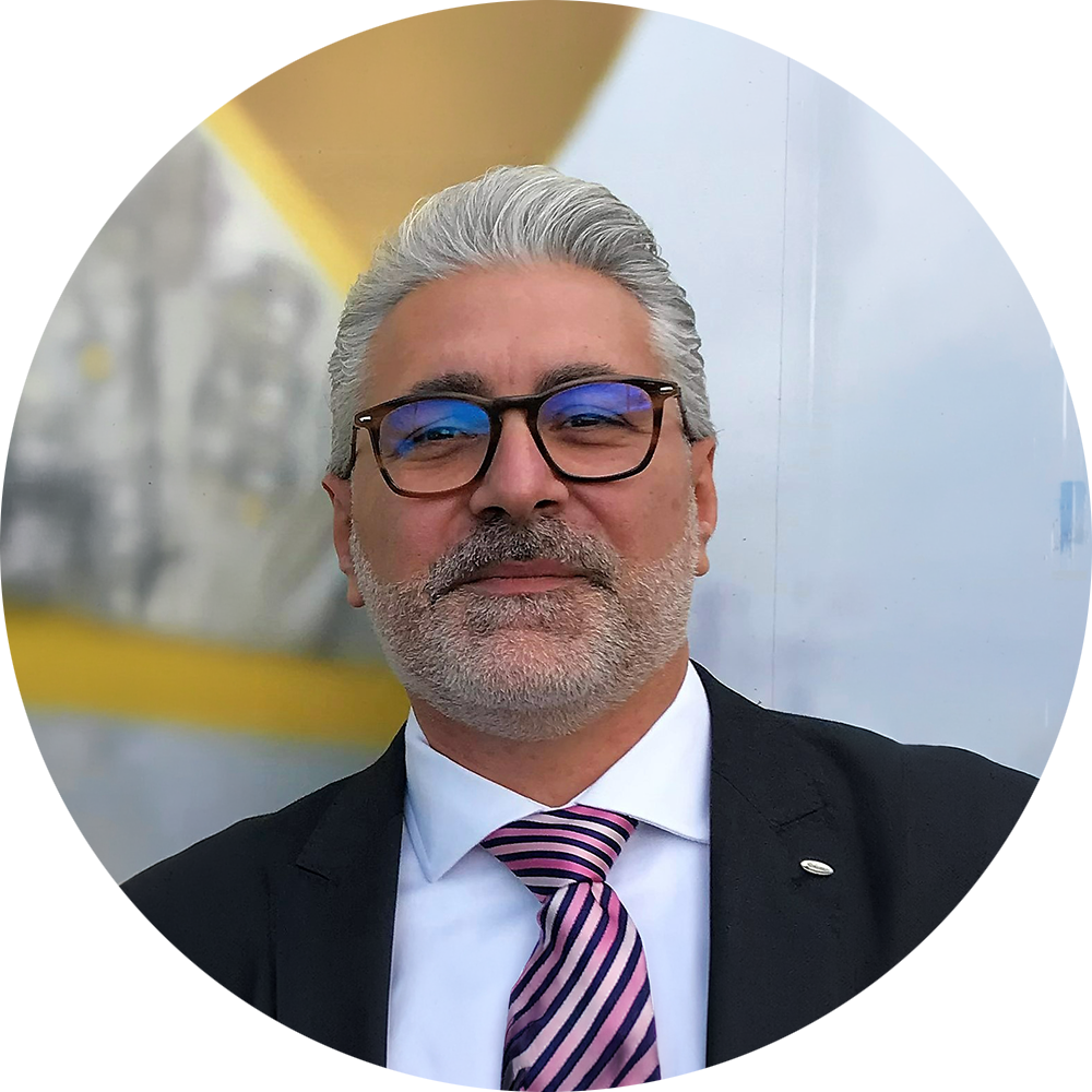 一个有着灰色头发和眼镜的男人，穿着一套带条纹领带的西装。背景模糊而明亮。