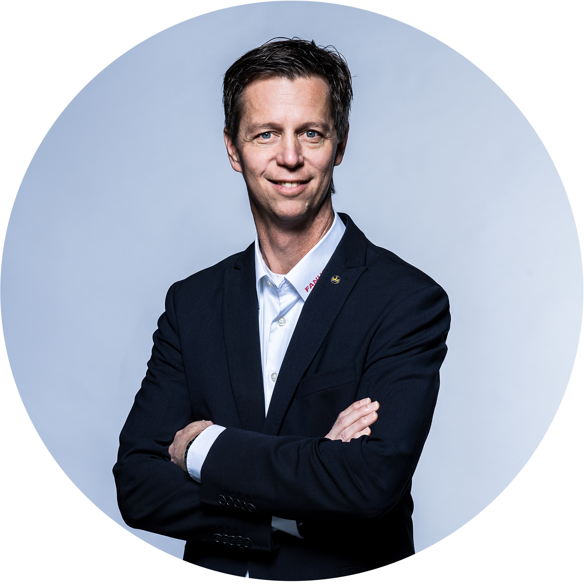 一个穿着黑色西装、双臂交叉的男人对着镜头微笑。背景明亮而中性。