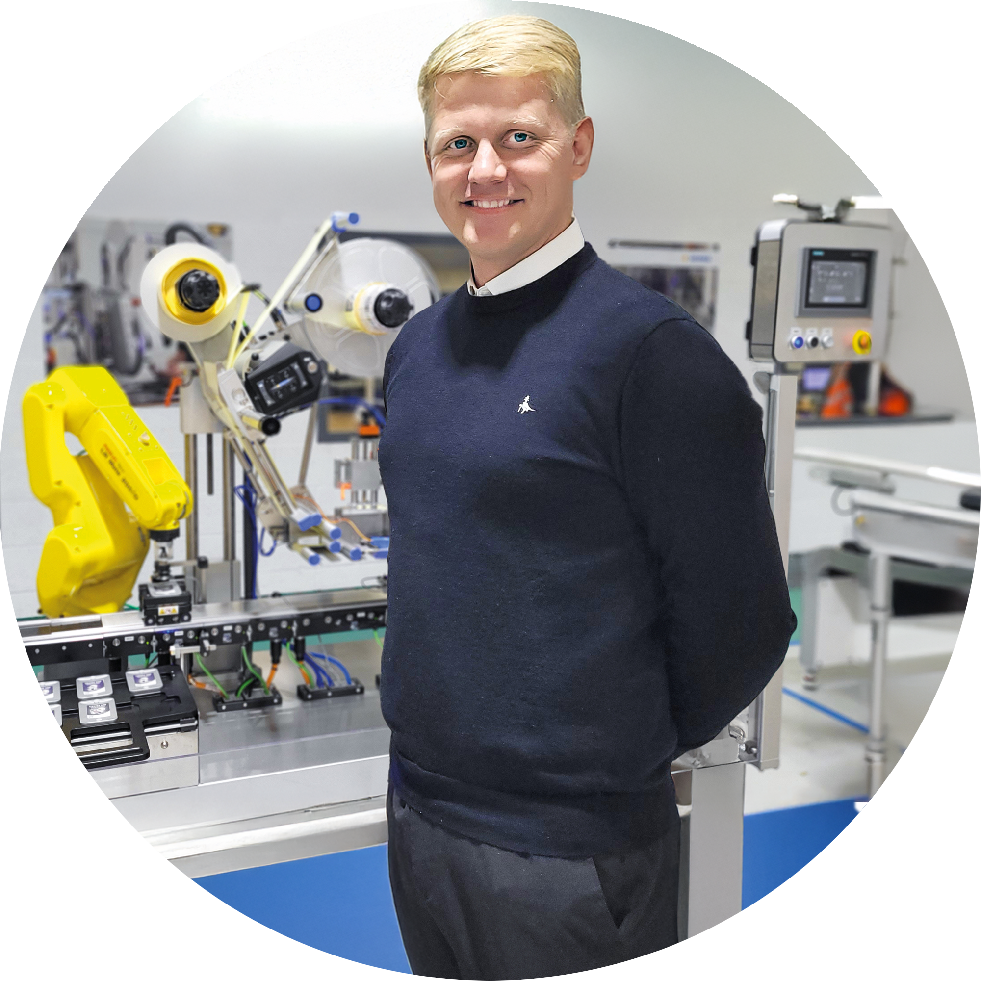 一个穿着黑色毛衣的男人站在一条配备机器人和技术设备的自动化生产线上。