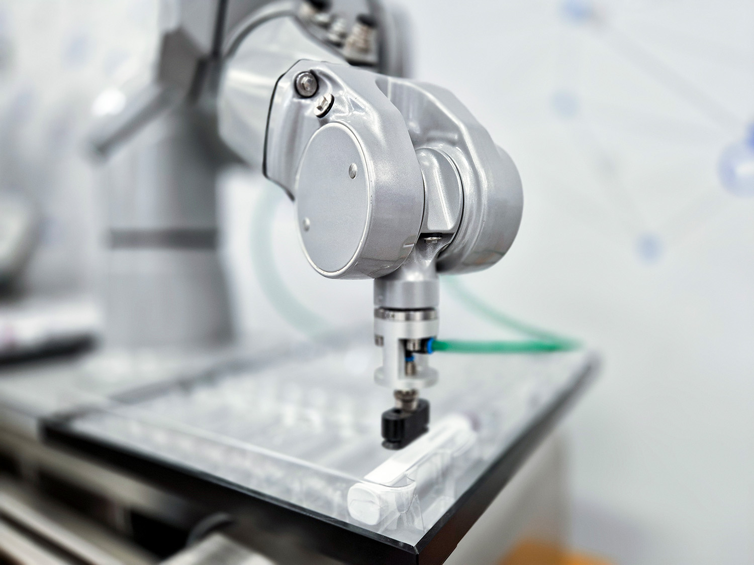 工业机器人手臂配有抓手，正位于一个透明的表面上，准备抓取一个物体。