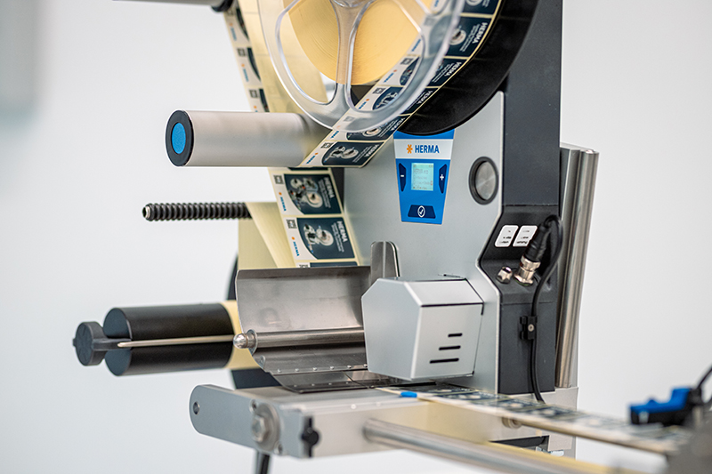 Eine Etikettiermaschine mit Rollen, Steuerungselementen und einem Display zur Anpassung der Einstellungen.