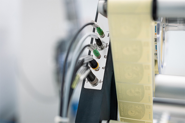 Steuerungseinheit mit mehreren Anschlüssen und einer Rolle mit Etiketten in einem industriellen Umfeld.