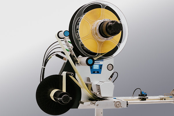 Eine Maschinenkomponente mit einer großen Spule gelbem Material, verbunden mit Schläuchen und einem Steuerpanel, zur Verarbeitung oder Verpackung.