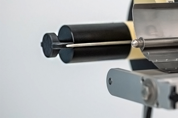 Nahaufnahme eines Geräts mit zwei Rollen und einer Nadel, die für präzise Anwendungen in der Fertigung oder Technik verwendet wird.