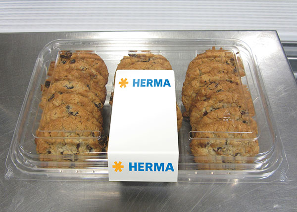 Eine transparente Verpackung mit mehreren Schokoladenkeksen, in der Mitte mit einem weißen Etikett mit der Aufschrift "HERMA".