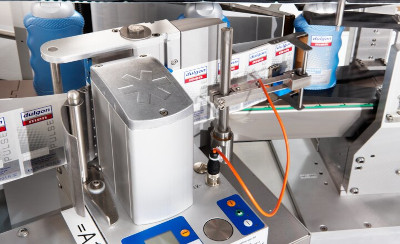 Maschine zur Etikettierung von Flaschen mit präzisen Steuermechanismen und digitalen Anzeigen. Flaschen in verschiedenen Farben sind sichtbar.