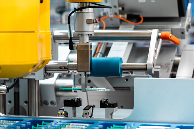 Industrieroboter mit gelbem Arm, der an einer Fertigungsstation arbeitet, um elektronische Komponenten zu montieren.