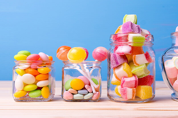 Bunte Süßigkeiten in verschiedenen Gläsern auf einem Holzuntergrund, mit einem blauen Hintergrund.