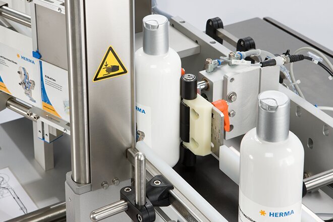 Eine Abfüllmaschine mit weißen Flaschen auf einem Förderband, ausgestattet mit verschiedenen technischen Komponenten und Warnhinweisen.