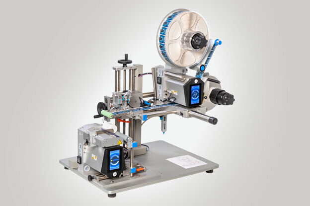 Eine Etikettiermaschine mit verschiedenen Komponenten zur Anwendung von Etiketten auf Produkte. Sie ist auf einem stabilen Tisch montiert.